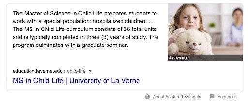 Smiling child holding a white teddy bear, sitting at a table with a blurred background.