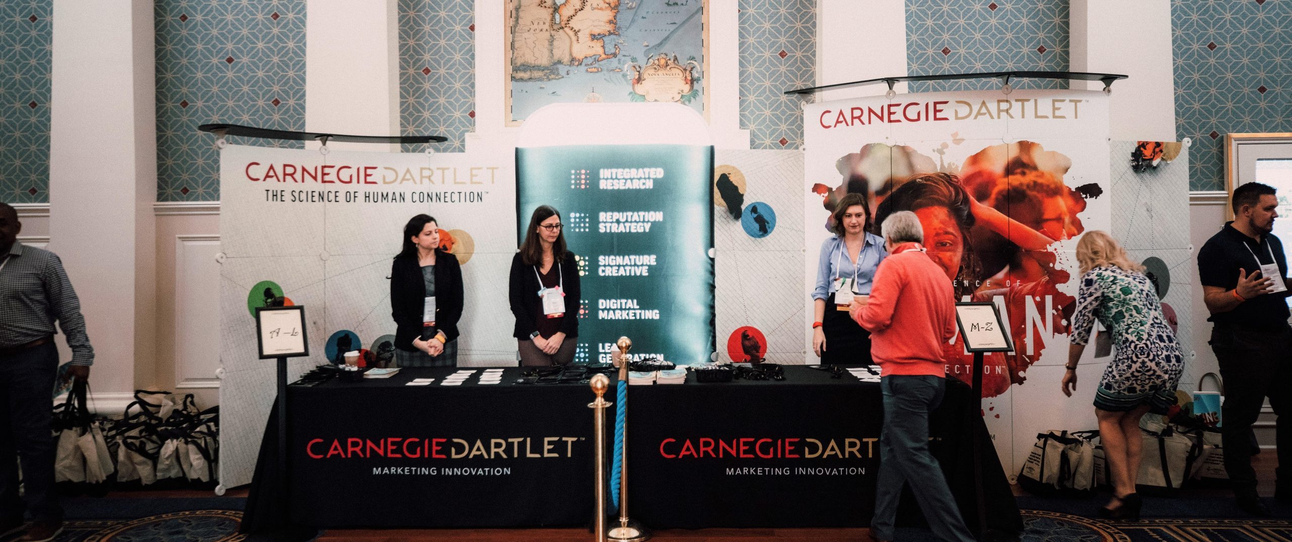 Carnegie conference booth. Carnegie employees engaging with visitors with Carnegie banners in the background