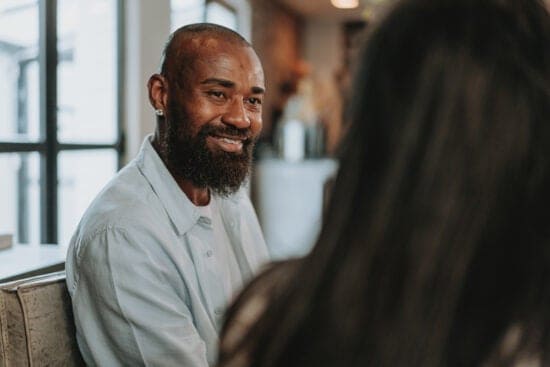 Smiling man with a beard talks to a woman in a brightly lit indoor setting, discussing student search opportunities.