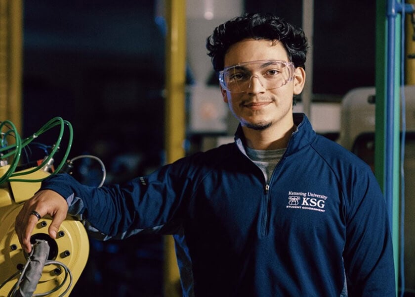 A man wearing safety goggles stands beside industrial equipment.