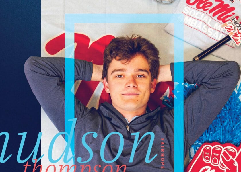 Young man lying on a bed with Ole Miss fan items, smiling with hands behind his head.