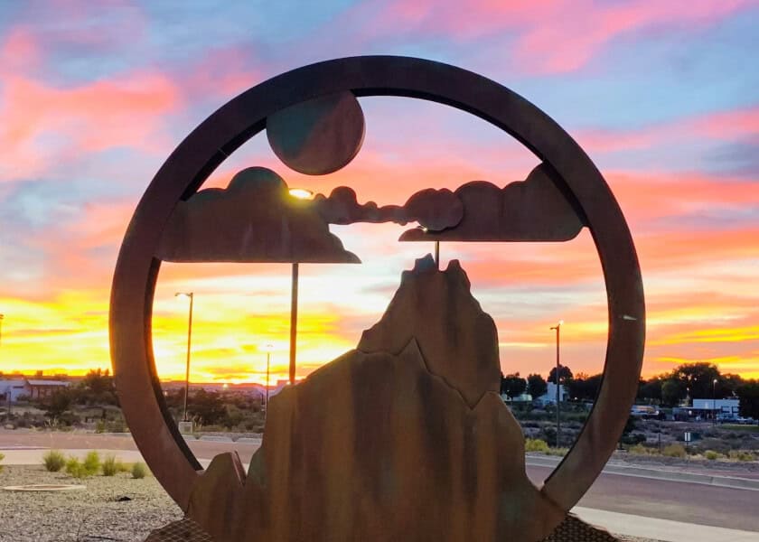 Metal sculpture of mountains and clouds with a colorful sunset sky in the background.