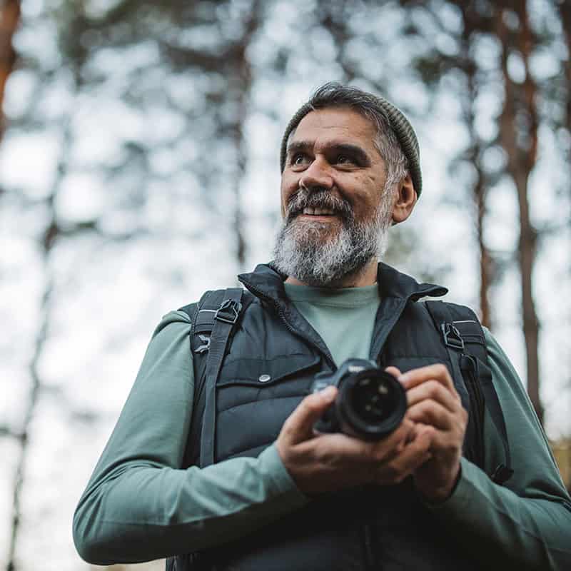 Man smiling with camera in the woods