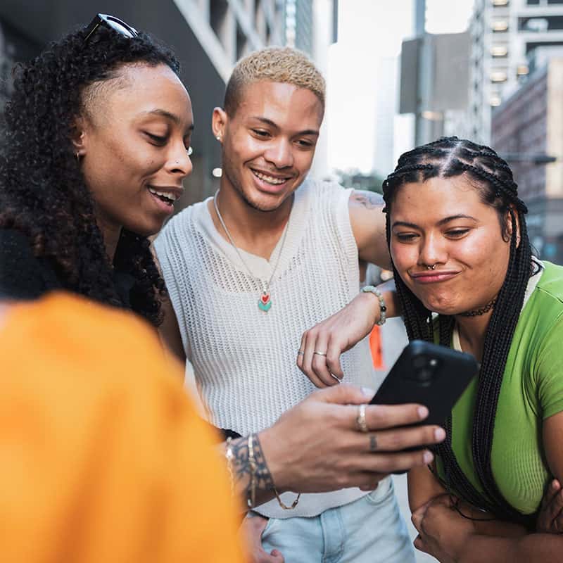 Three young adults taking a selfie surrounded by tall buildlings