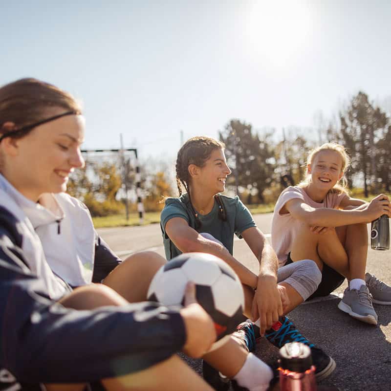 Three women sitting outdoors with soccer ball