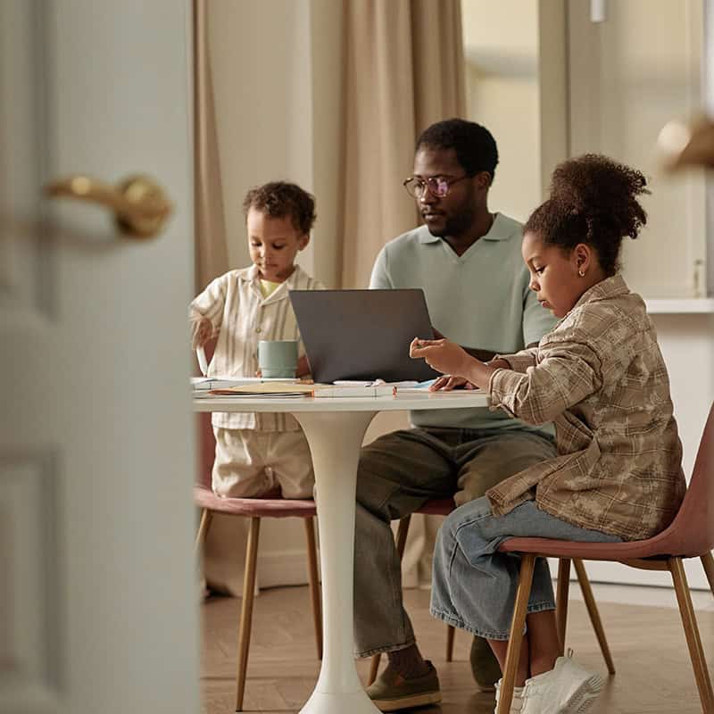 Father and two children doing work at kitchen table