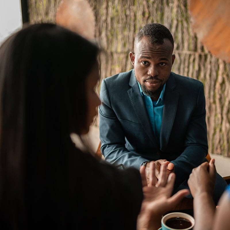 Man with hands clasped in discussion with two women.