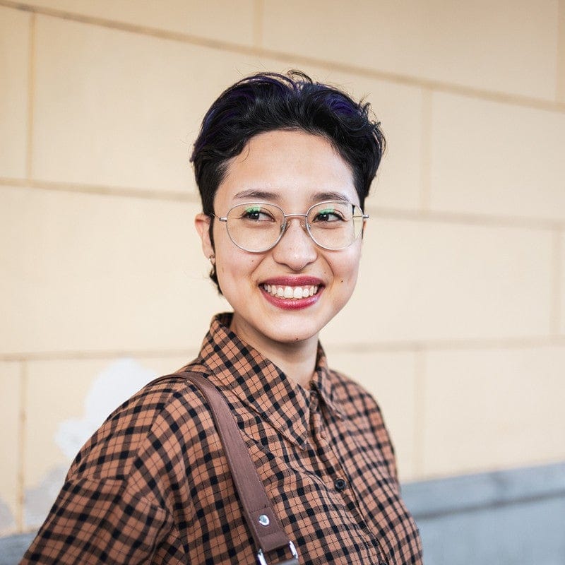 Person with short hair and glasses, smiling in a plaid shirt, standing in front of a beige wall—ready to tackle enrollment management challenges.