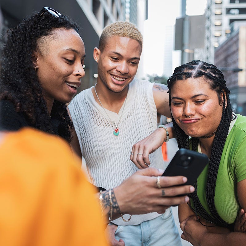 Three young adults taking a selfie surrounded by tall buildlings