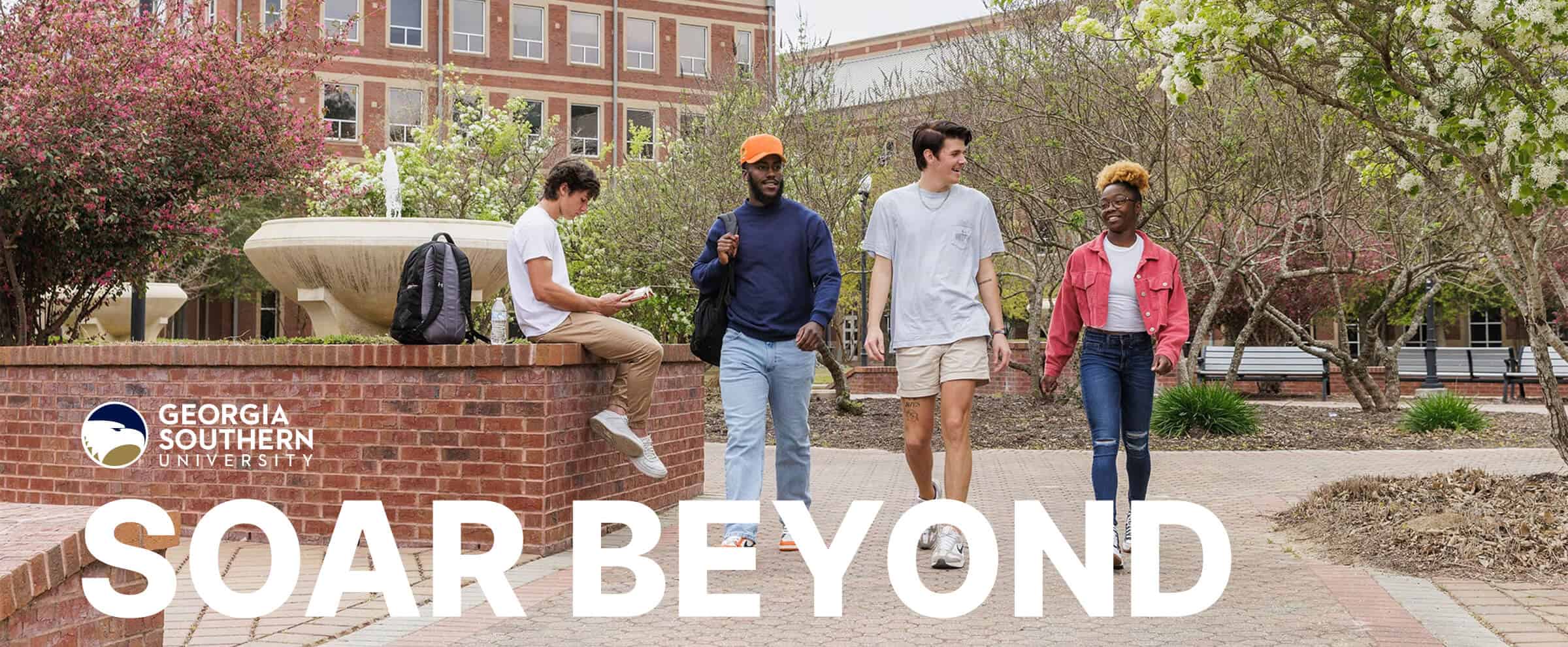 Four students walk and talk on a university campus surrounded by trees, with "SOAR BEYOND" text in front.