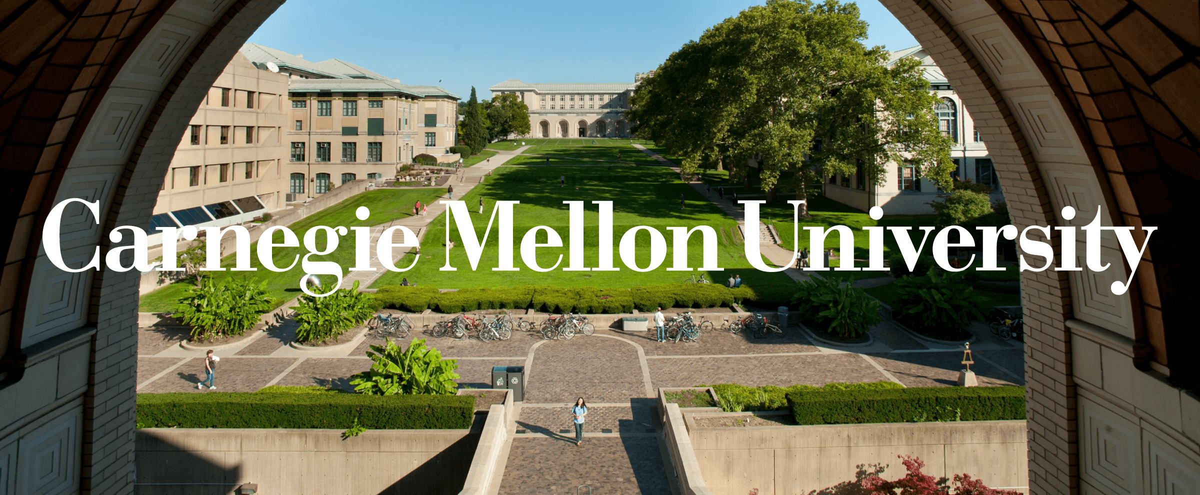 View of Carnegie Mellon University campus courtyard with green lawns, trees, and academic buildings on a sunny day.