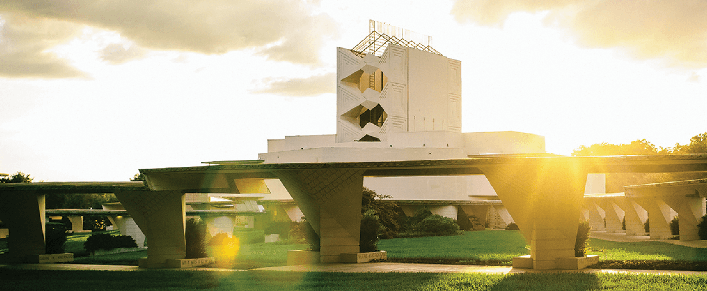 A modern white building with geometric shapes, sunlight streaming through, and green lawns in the foreground.