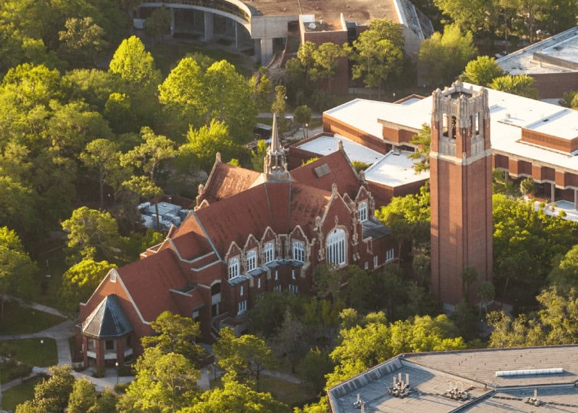 Aerial view of a red-roofed historic building and clock tower surrounded by trees on a campus.