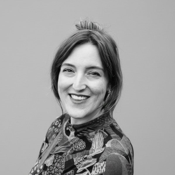 Smiling woman with medium-length hair in a patterned top, posing against a plain background. Black and white photo.