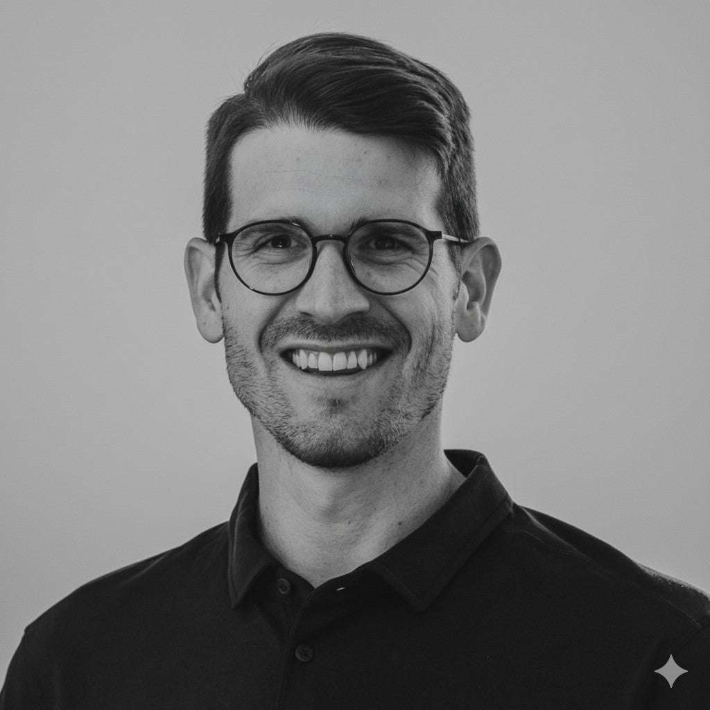 Smiling man with glasses and short hair wearing a dark collared shirt against a plain background.