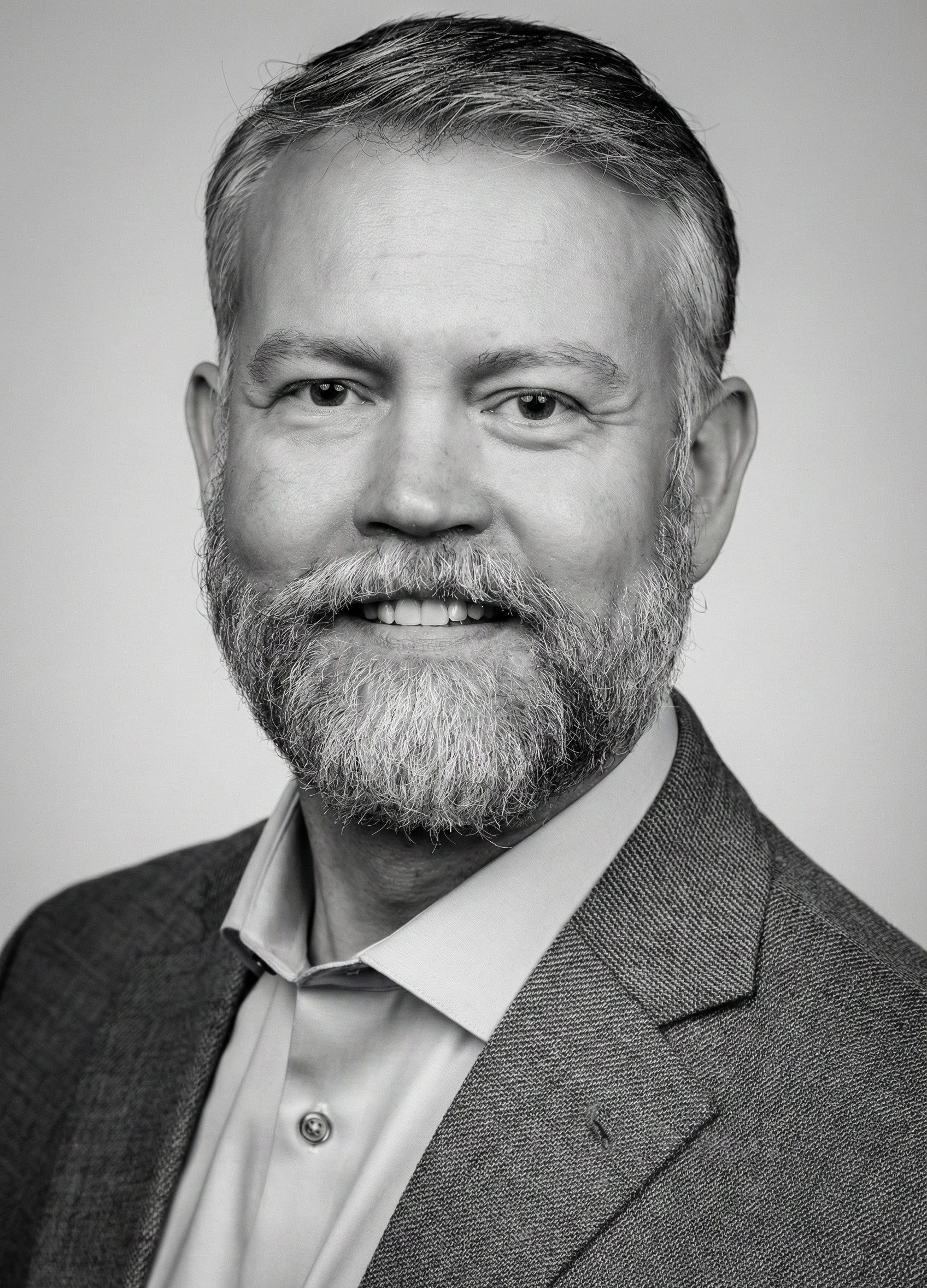 Black and white portrait of a smiling bearded man in a suit jacket and collared shirt.