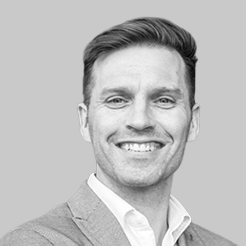 Smiling man in a suit jacket and white shirt, against a plain grey background.