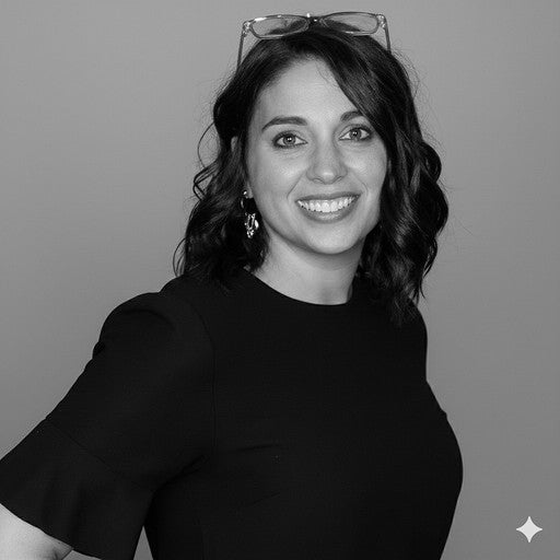 Woman with wavy hair, wearing glasses on her head, smiling, in a black top against a plain background.