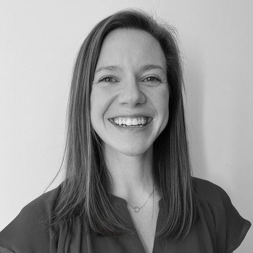 Smiling woman with straight hair wearing a dark top, photographed against a plain background in black and white.