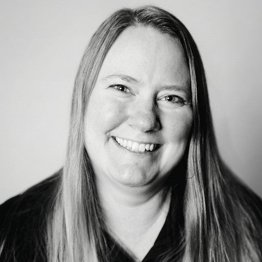 Smiling woman with long straight hair, wearing a dark top, in a black and white portrait.