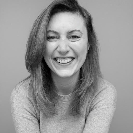 Woman with shoulder-length hair smiling and laughing, wearing a light sweater, against a plain background.