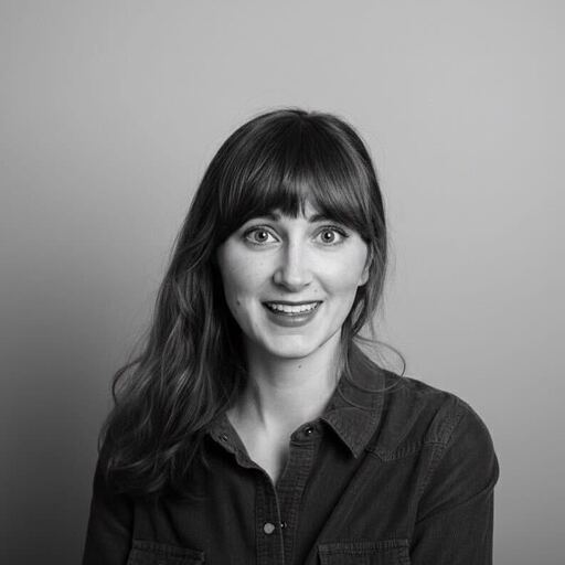 A woman with long hair and bangs smiles at the camera against a plain background, in black and white.