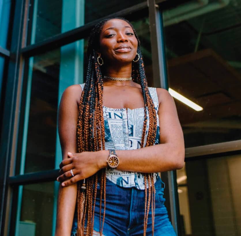 A woman with braids standing in front of a glass building.