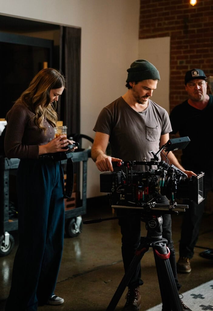 A man adjusts a film camera while a woman and another man stand nearby in a studio setting.