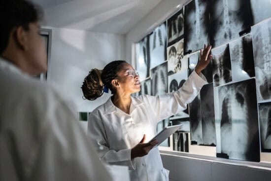 Doctor examining and discussing X-ray images on a wall display with a colleague in a medical setting.