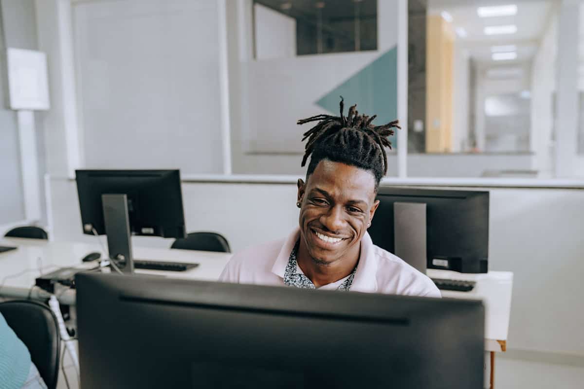 Man smiling while working at a computer in a modern office with multiple computer monitors.