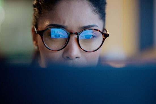 Woman wearing glasses intently looking at a computer screen, with reflections visible in her lenses.