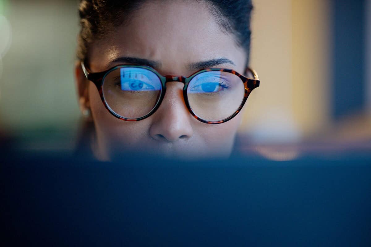 Woman wearing glasses intently looking at a computer screen, with reflections visible in her lenses.