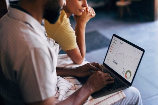 Two people viewing data charts and graphs on a laptop screen while sitting together indoors.