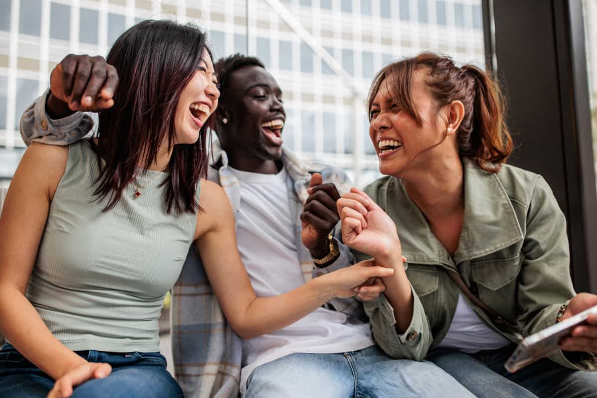 Three friends sitting close together, laughing and enjoying each other's company outdoors.