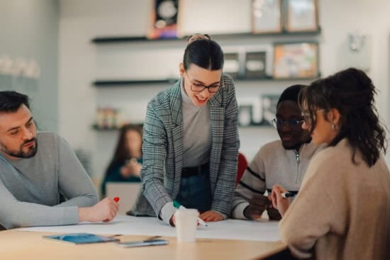Four people collaborate at a table, discussing ideas and writing on a large sheet of paper.