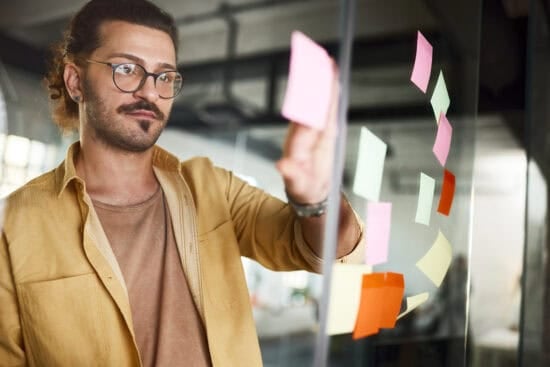 Man placing colorful sticky notes on a glass wall in a modern office setting.