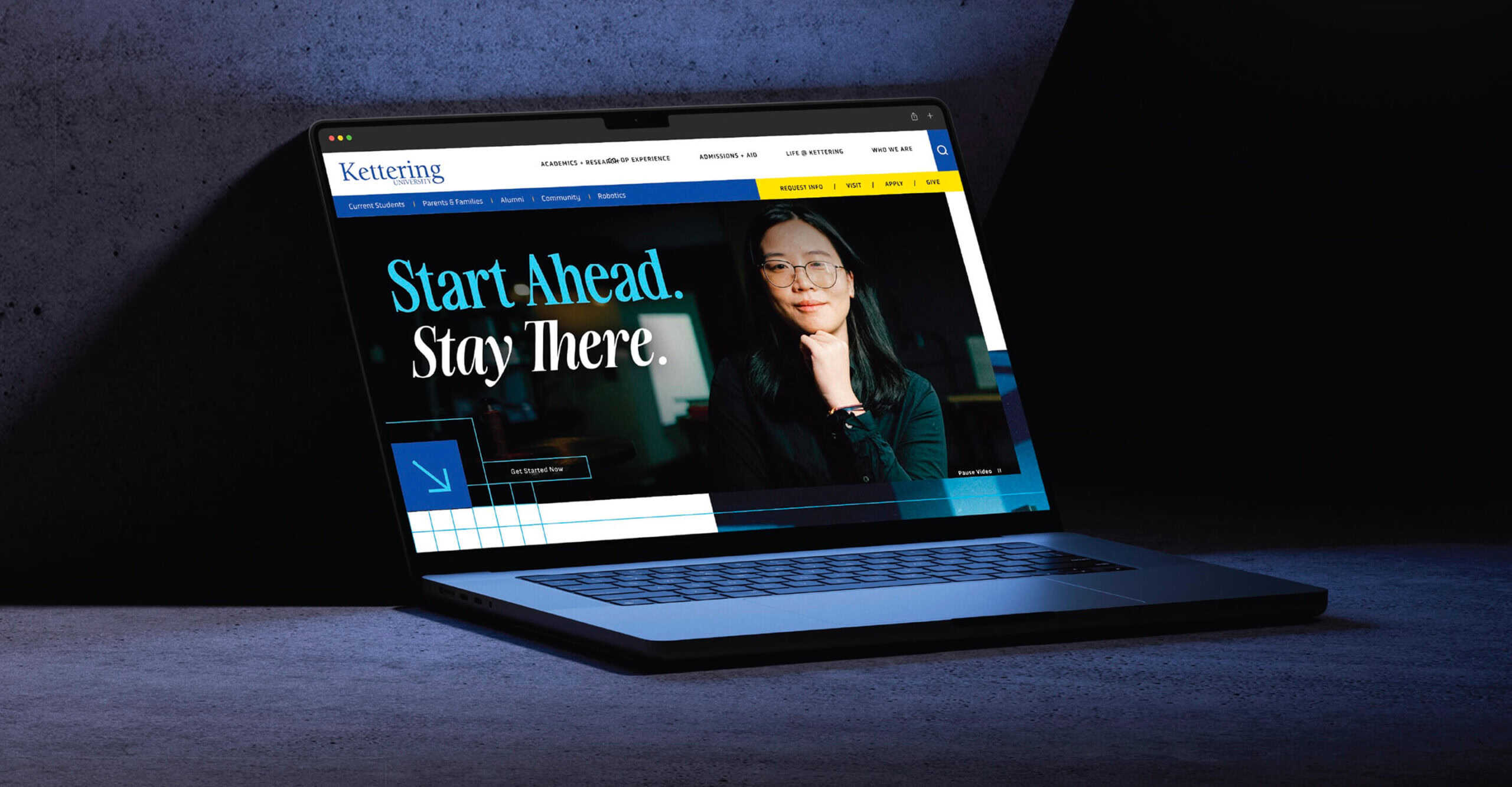 Laptop displaying Kettering University website with "Start Ahead. Stay There." and a woman smiling on screen.