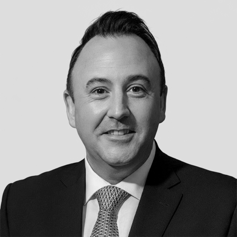 Smiling man in a suit and tie, facing forward against a plain light background.