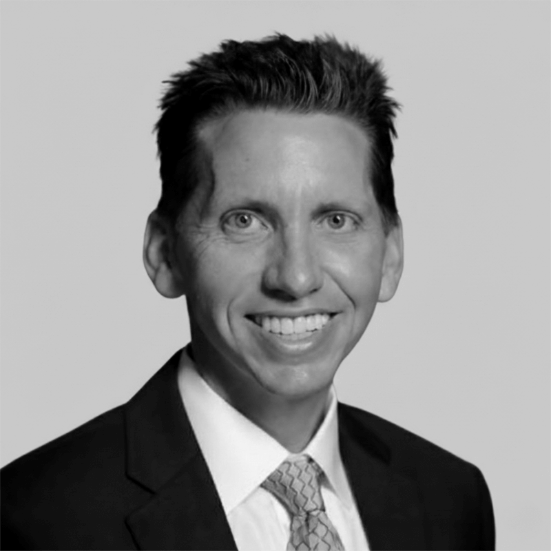 Smiling man in a suit and tie with short hair, photographed against a plain light background.