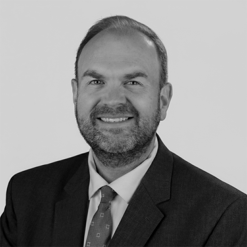 Smiling man in a suit and tie posing for a professional headshot against a plain background.