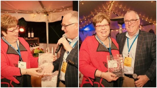 Two people at an event; woman receives an award, then poses for a photo with the man under string lights.