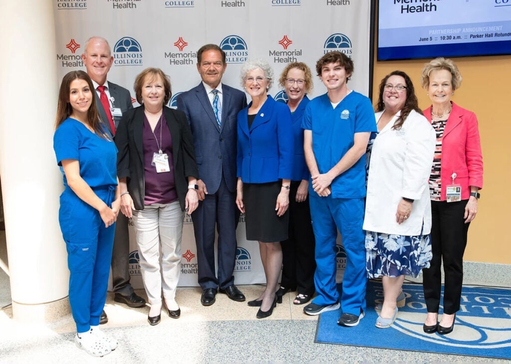A group of people, including students in scrubs, pose together at an Illinois College and Memorial Health event.