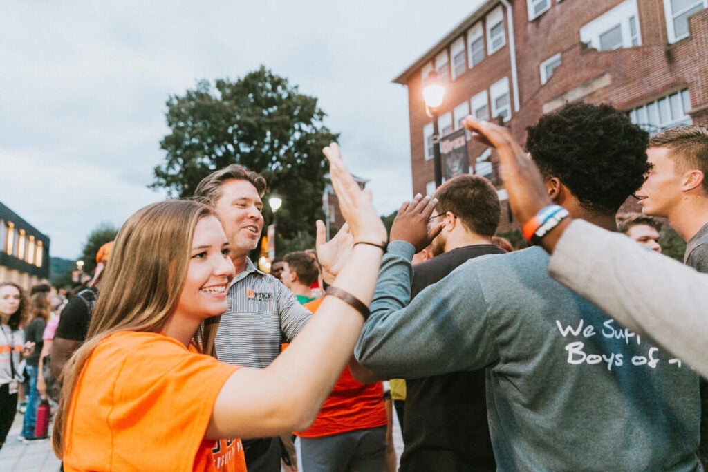 Students gathered outside a building, smiling and giving high fives during a campus event.