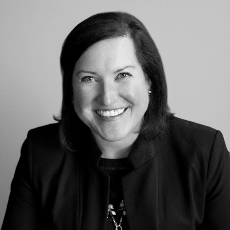 A woman in a dark blazer smiling at the camera against a plain, light background.