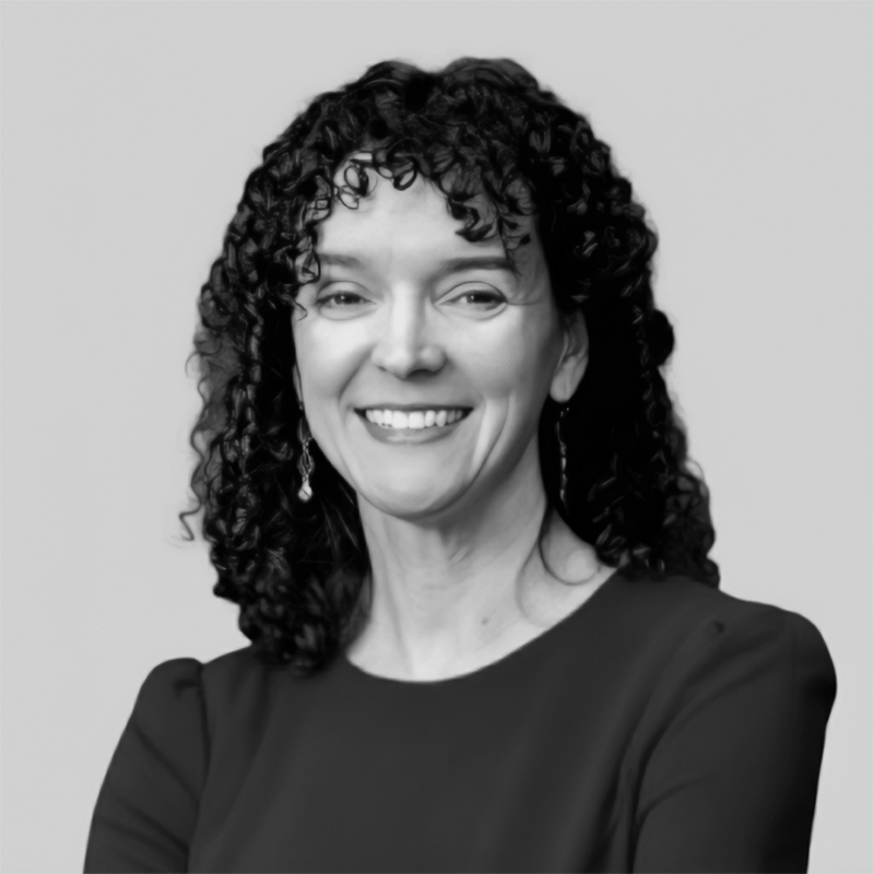 Smiling woman with curly dark hair wearing earrings and a dark top against a plain background.
