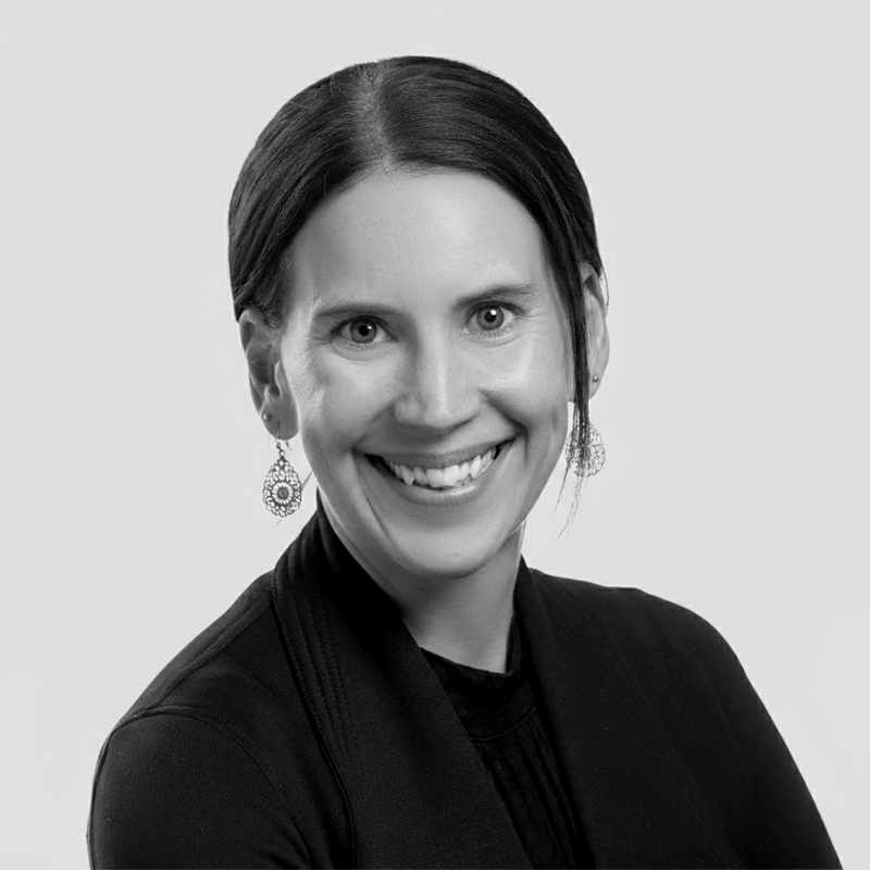 Smiling woman with dark hair, wearing earrings and a black top, in a black-and-white portrait.