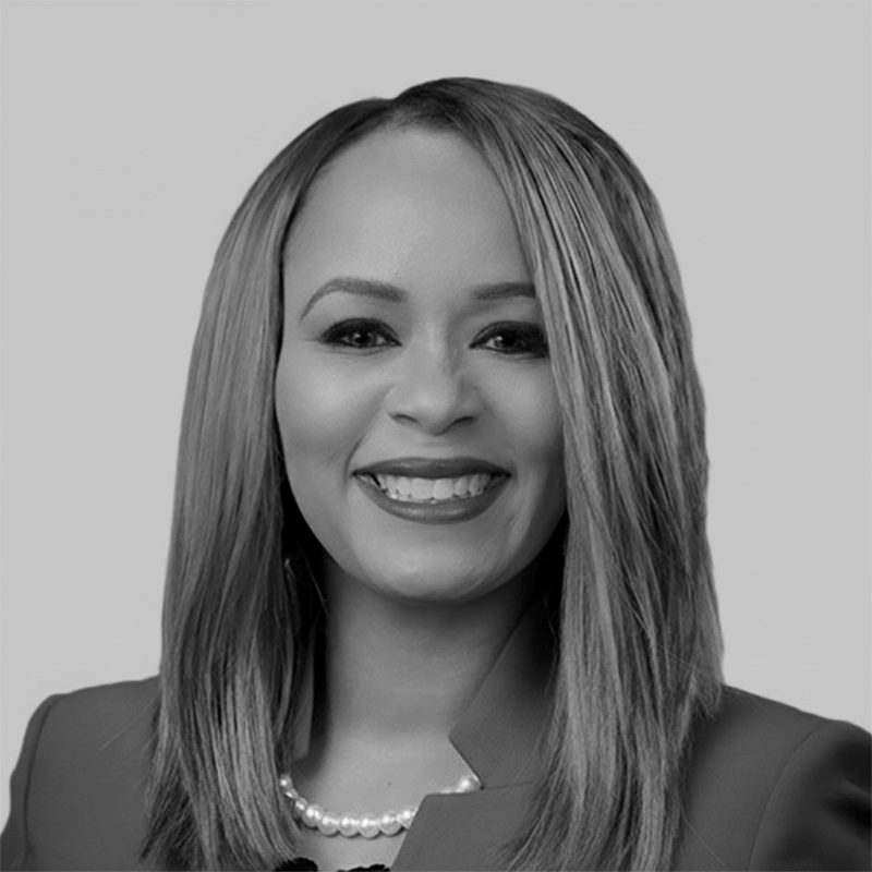 Smiling woman with straight hair, wearing a blazer and pearl necklace, against a plain background.