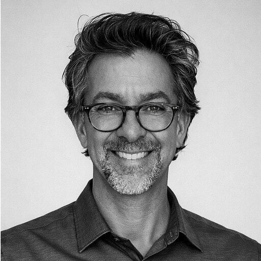 A man with glasses and gray hair smiling at the camera, wearing a dark collared shirt.
