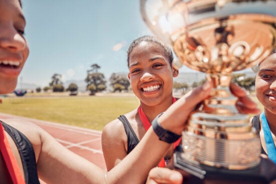 Smiling young athletes holding a large gold trophy on a track, wearing medals around their necks.