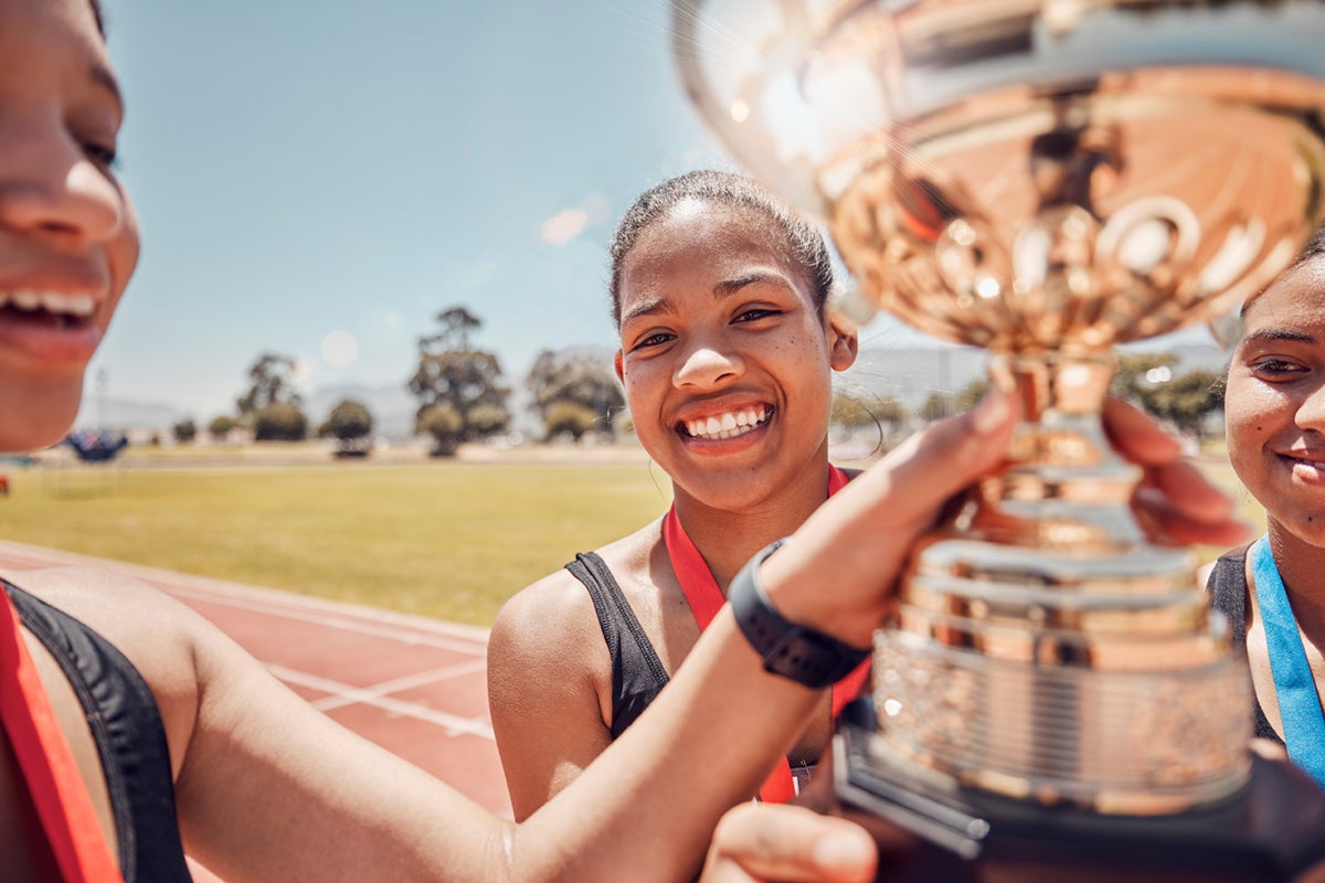 Smiling young athletes holding a large gold trophy on a track, wearing medals around their necks.